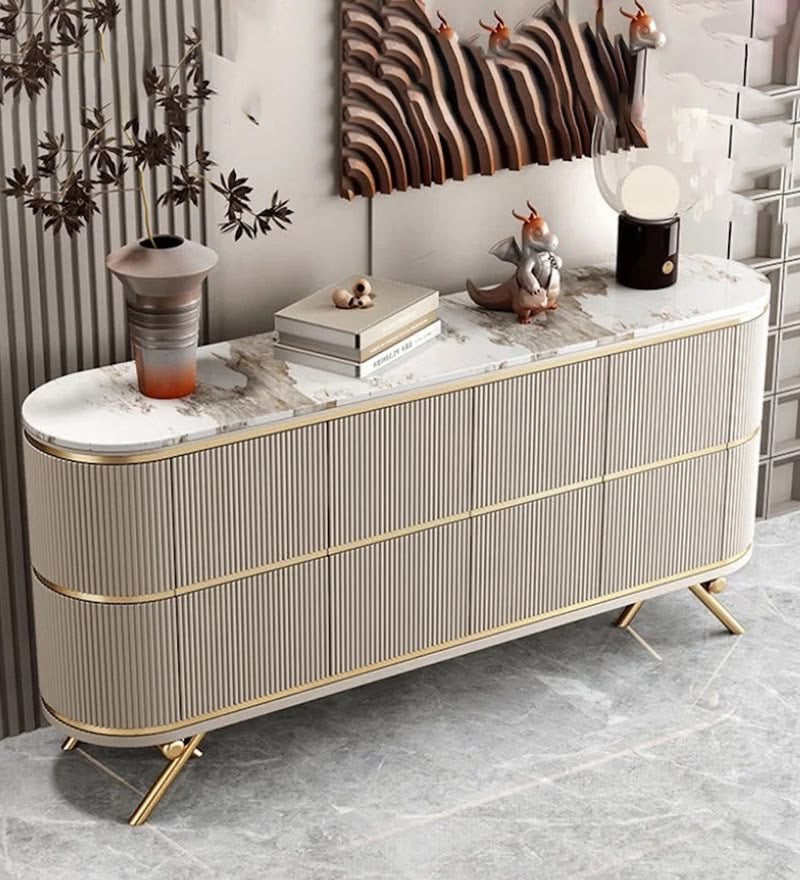 A modern long console cabinet with ribbed beige doors, gold trim, and a white marble top, styled in a contemporary interior with decorative objects on top.