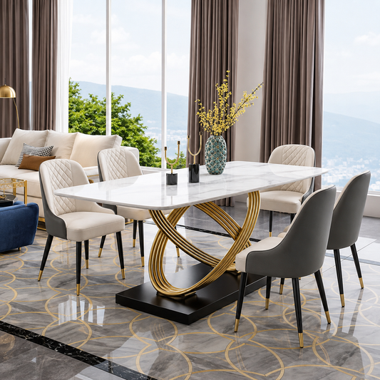 A modern dining room set featuring a rectangular white marble-top table with a sculptural gold metal base, surrounded by six upholstered dining chairs in cream and gray, set on a patterned marble floor with a large window in the background.