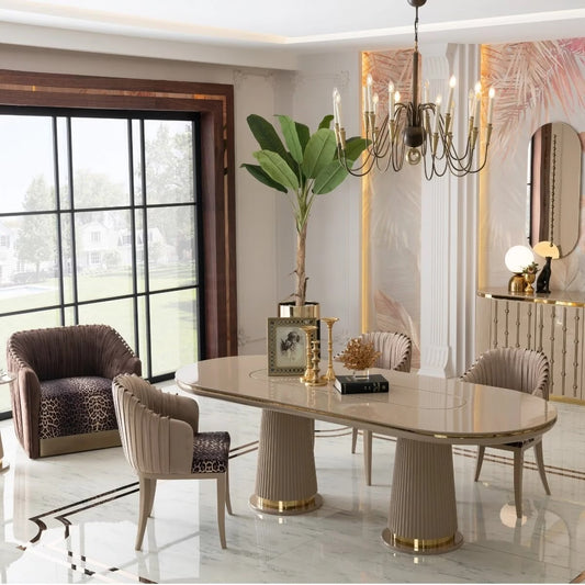 A modern dining room featuring a glossy oval dining table with fluted pedestal legs and matching upholstered chairs, styled in a luxurious interior with a chandelier, large windows, and decorative accents.