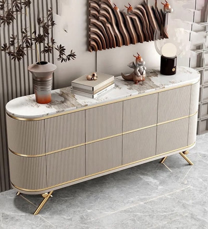 A modern long console cabinet with ribbed beige doors, gold trim, and a white marble top, styled in a contemporary interior with decorative objects on top.
