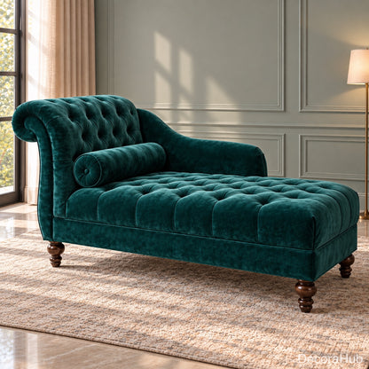 A classic chaise lounge in deep emerald green velvet, featuring a tufted backrest and seat cushion with a matching cylindrical pillow, set on a textured beige rug in a styled room with a window and warm lighting.