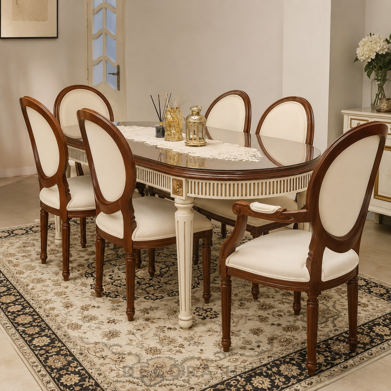 An eight-piece dining set including an oval table with a glass top and white pedestal legs, surrounded by six matching chairs with cream upholstered seats and backs, shown on a patterned area rug in a dining room setting.