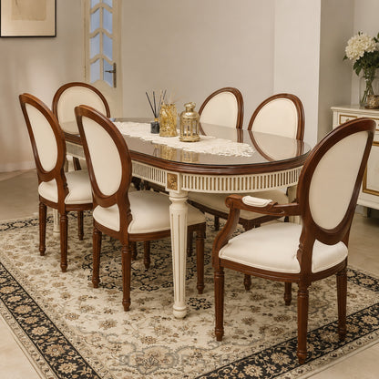 An eight-piece dining set including an oval table with a glass top and white pedestal legs, surrounded by six matching chairs with cream upholstered seats and backs, shown on a patterned area rug in a dining room setting.