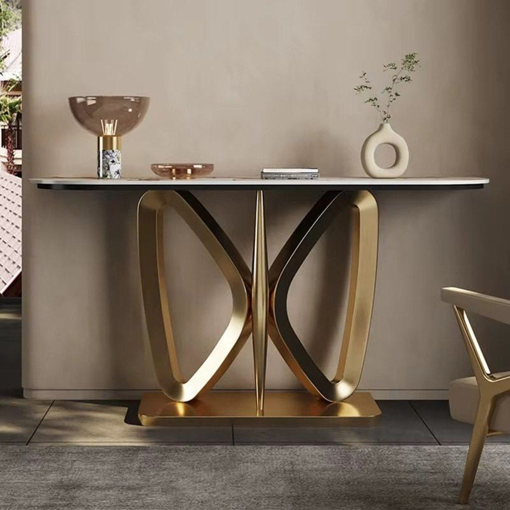A modern console table with a white marble-look top and sculptural gold metal base, styled in a minimalist interior with decorative objects on top.