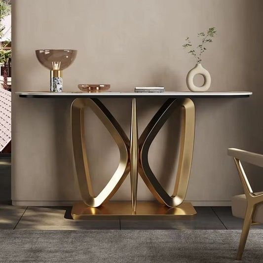 A modern console table with a white marble-look top and sculptural gold metal base, styled in a minimalist interior with decorative objects on top.