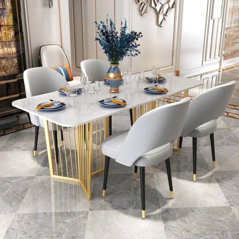 A modern dining table set in a bright, elegant dining room. The table features a white marble-look top with a gold geometric wire base, surrounded by six light gray upholstered dining chairs with black legs and gold accents.