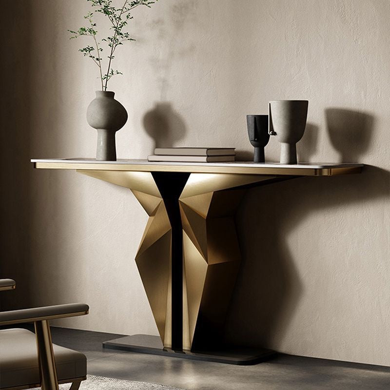 A modern console table with a geometric faceted gold pedestal base and a light wood top, styled in a minimalist room with a textured beige wall, decorative vases, and books.