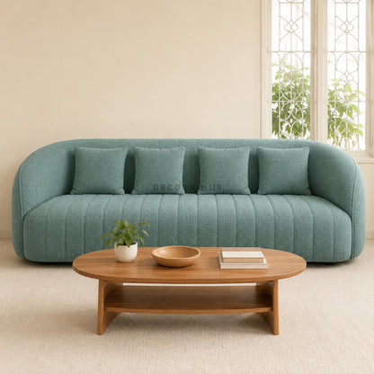 Teal sofa with cushions in a living room setting with a wooden coffee table.