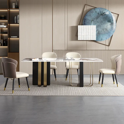A modern dining room setup featuring a rectangular white marble-top dining table with a black and gold pedestal base, surrounded by four upholstered dining chairs in beige and taupe tones, set on a textured light rug against a beige wood-paneled wall with decorative wall art.