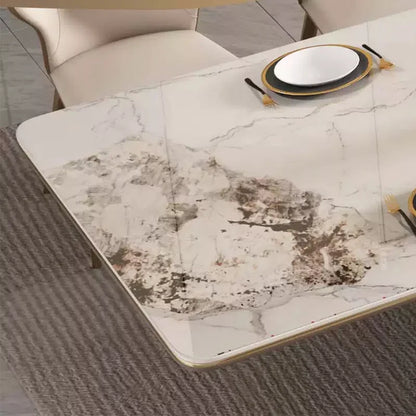 A rectangular dining table with a white marble-look surface featuring gray and brown veining, styled with plates and cutlery in a modern dining room setting.